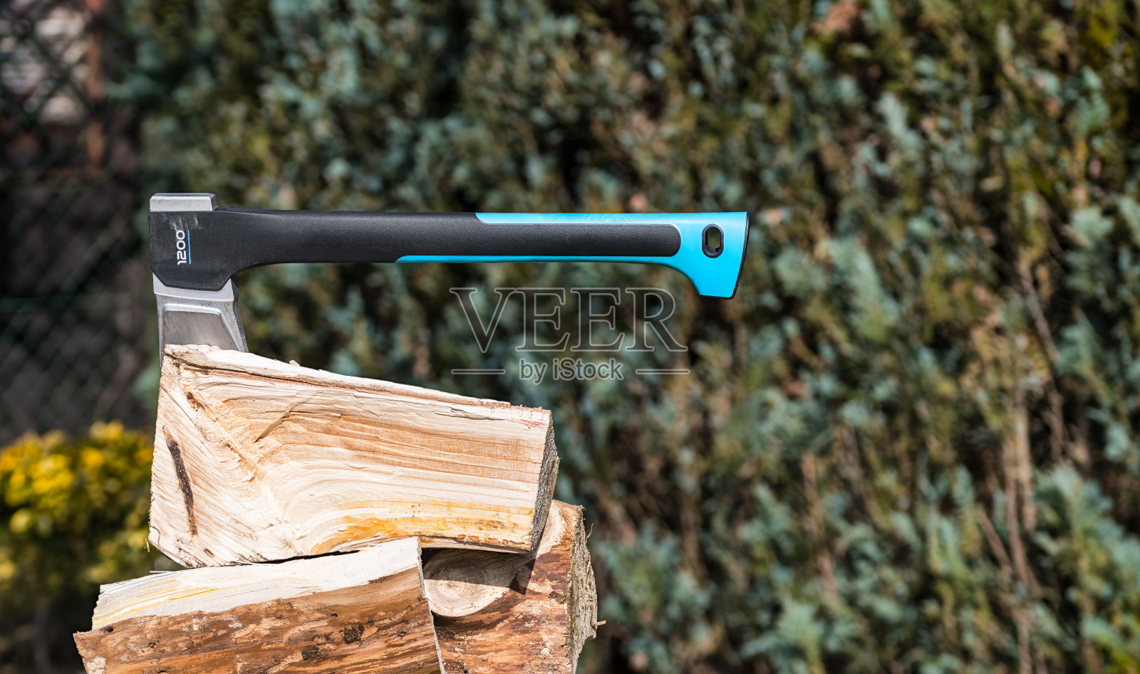 现代劈斧在花园树篱模糊的绿色背景上砍过的木头堆上照片摄影图片