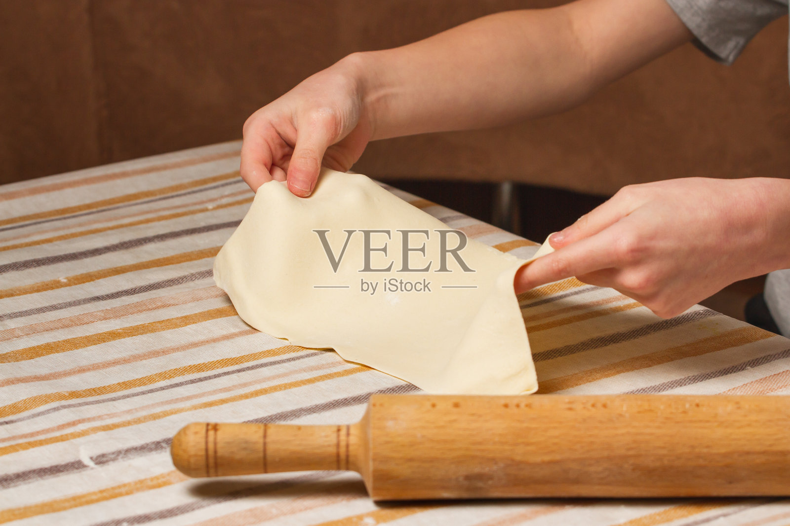 男孩的手在家里的厨房里用擀面杖擀面。照片摄影图片