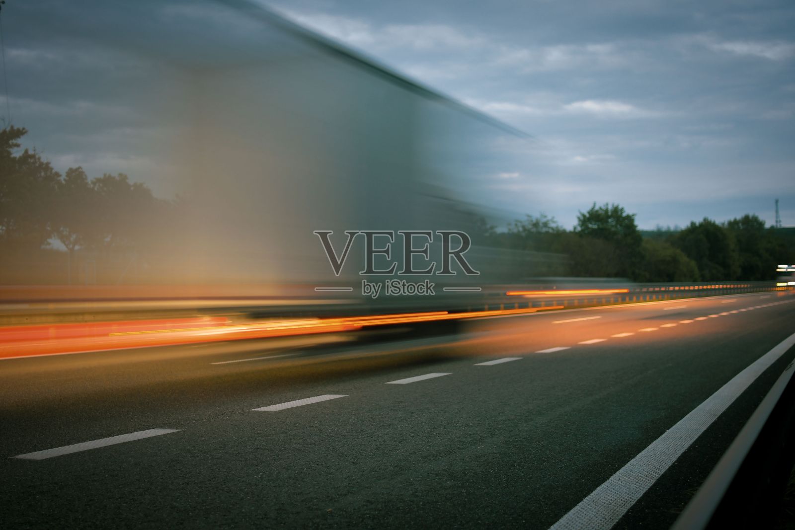 黄昏时一辆卡车行驶在高速公路上。高速公路上的动态模糊。一辆卡车的夜景。国际运输和物流的概念。照片摄影图片