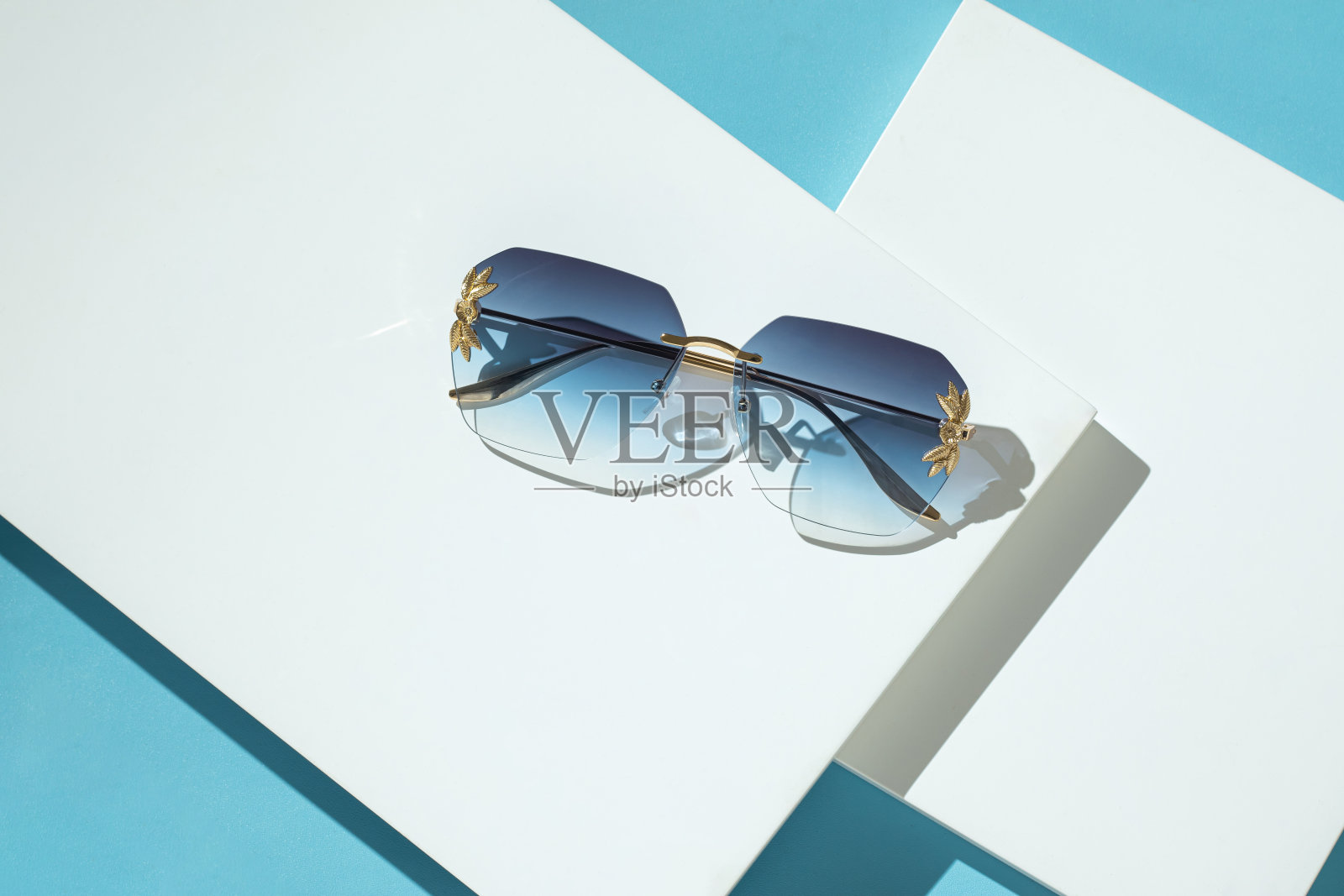时尚的蓝色方形太阳镜在白色和蓝色的背景。蓝色的表照片摄影图片