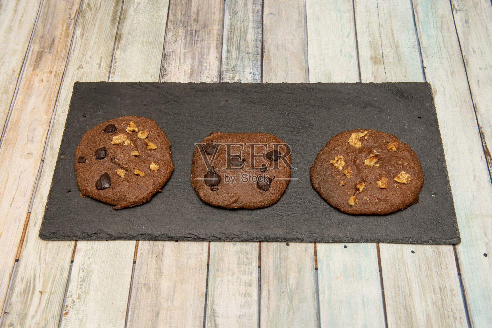 不同口味的巧克力饼干，用巧克力片、坚果片和干果片放在黑色石板盘上照片摄影图片