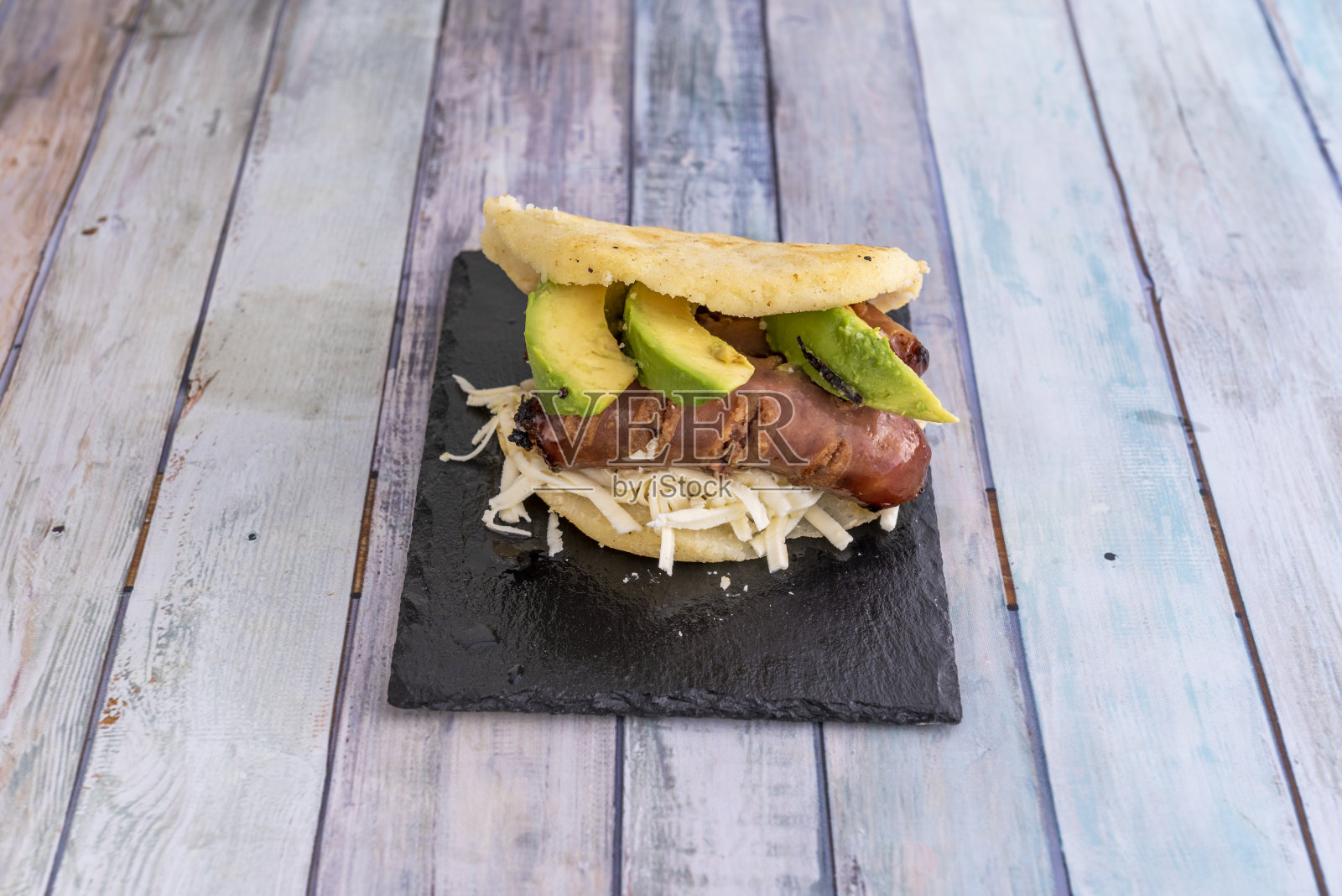 黑色石板盘上的西班牙薄饼配磨碎的新鲜奶酪和烤辣香肠和鳄梨照片摄影图片