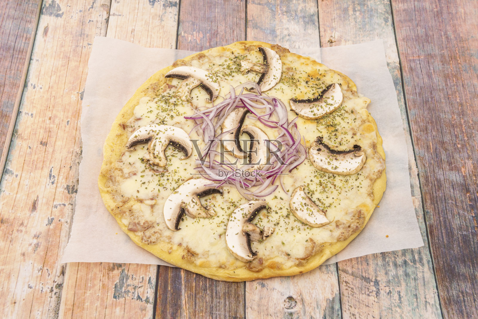 木质餐桌上的小比萨，加蘑菇片、红洋葱、马苏里拉奶酪和干牛至叶照片摄影图片