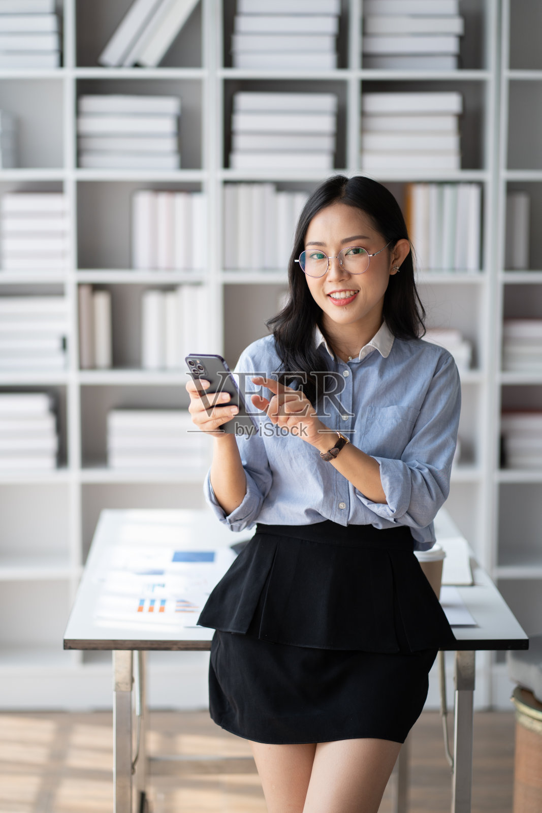 快乐的亚洲女商人在办公室工作时使用智能手机。照片摄影图片