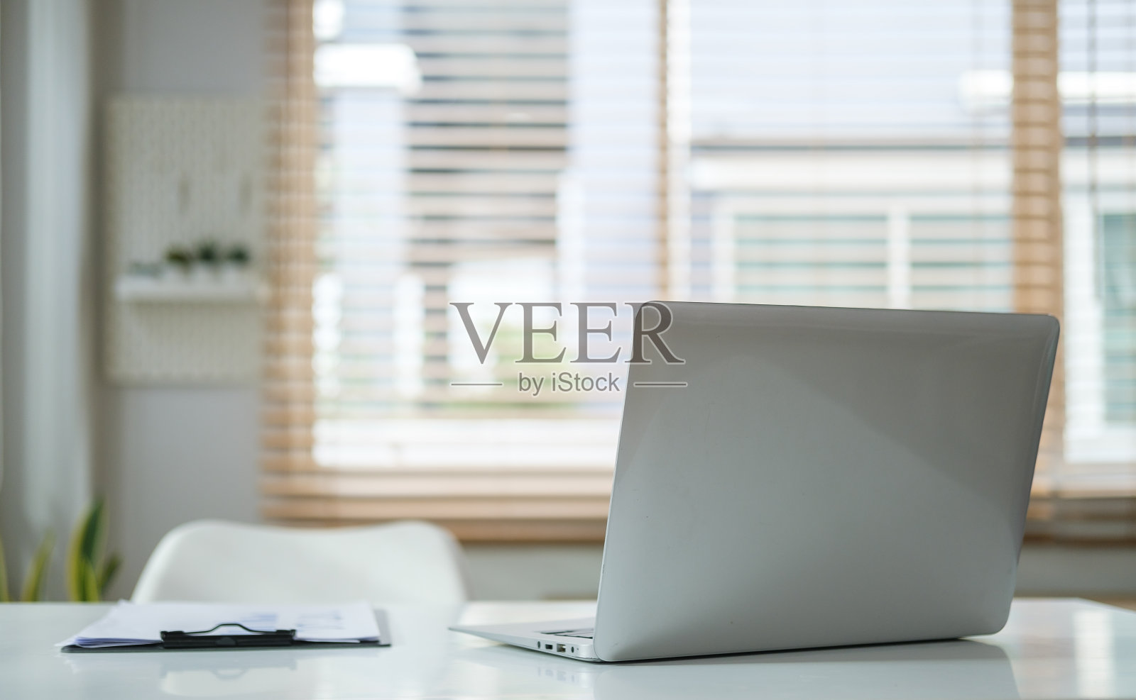 现代家庭办公室内部白色办公桌上的笔记本电脑和剪贴板。照片摄影图片