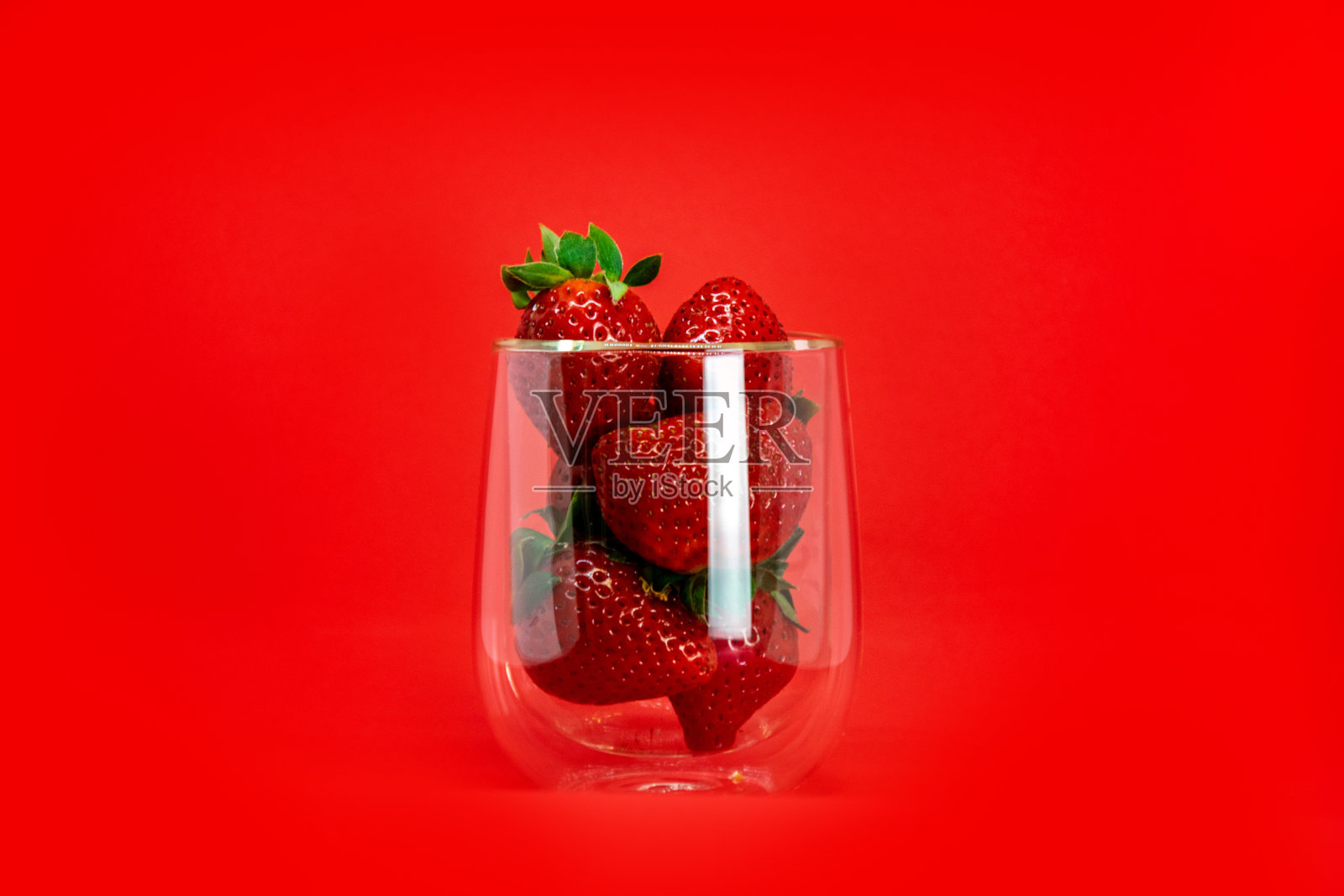 草莓放在红色背景的透明玻璃杯里。照片摄影图片