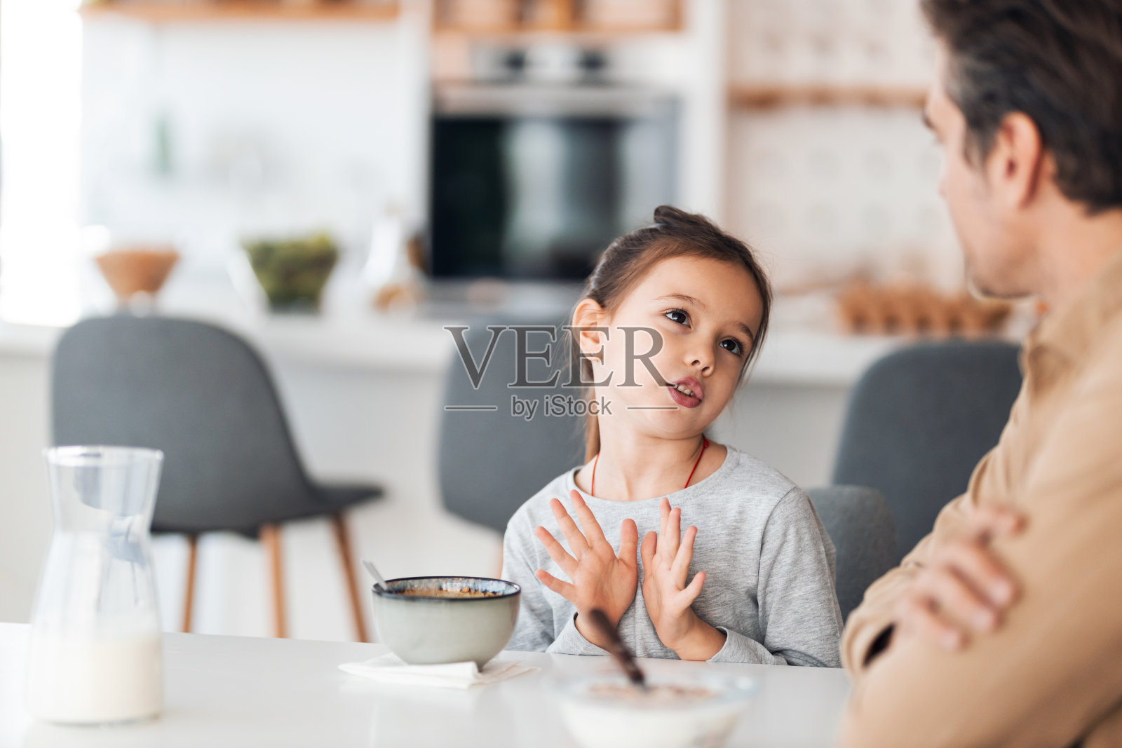 一个可爱的小女孩和她爸爸在家里吃早餐的时候聊天。照片摄影图片