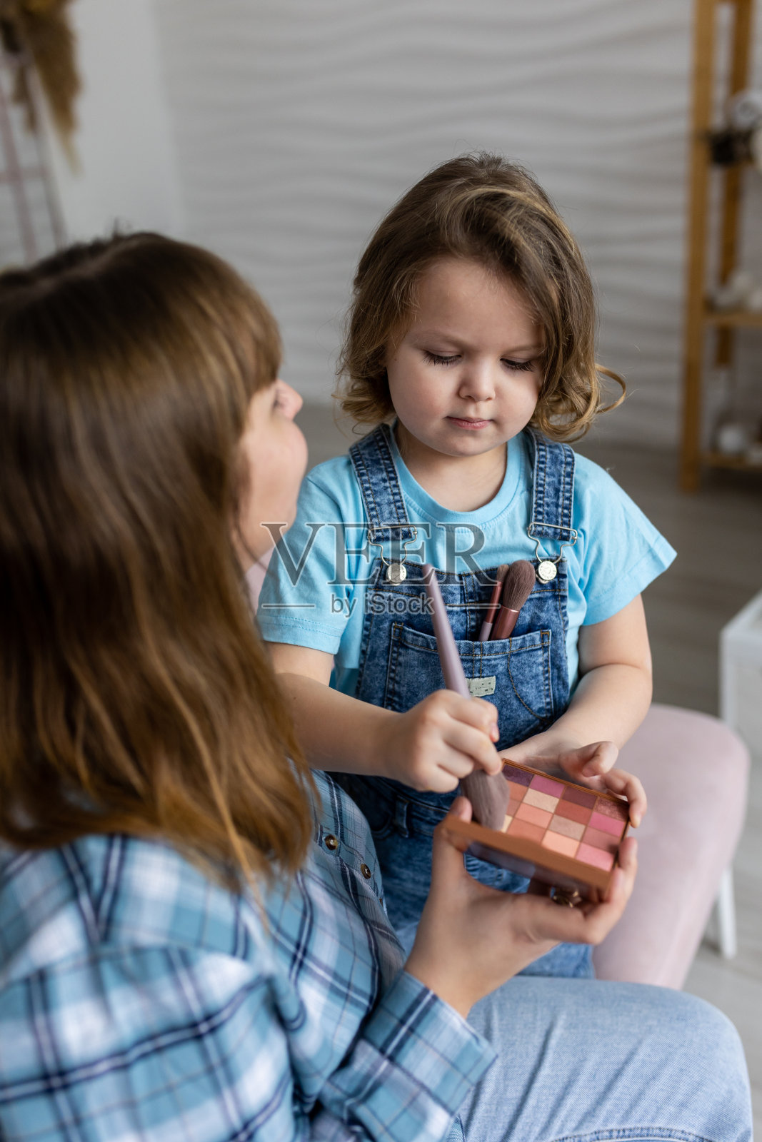 漂亮可爱的小女孩正在用眼影板和眼影刷给妈妈化妆。优质的家庭时光，享受家庭生活，为人母。妇女节或母亲节庆祝活动，一起玩乐照片摄影图片