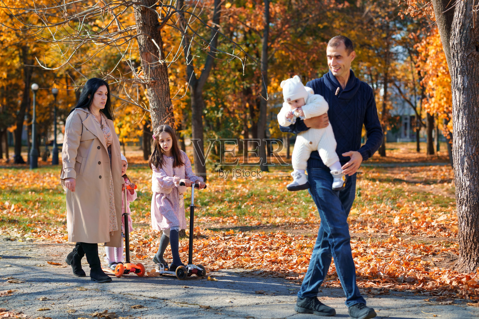 一个大家庭在秋天的城市公园里散步，孩子和父母，快乐的人们享受着美丽的大自然，明媚的阳光和黄色的树叶照片摄影图片