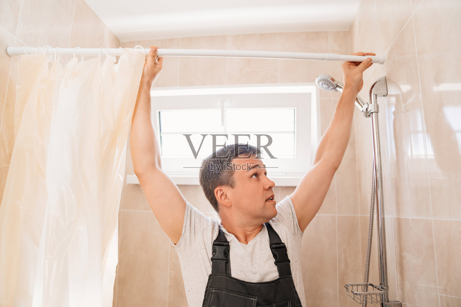 一位师傅在浴室里安装浴帘条。照片摄影图片