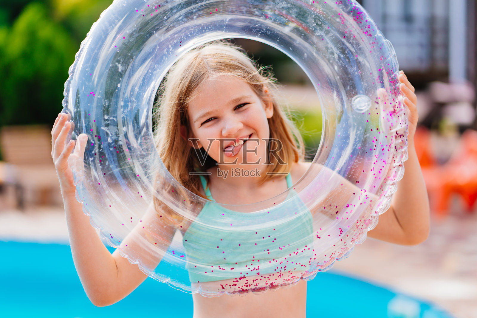 可爱有趣的十几岁的女孩穿着泳装和充气救生圈在游泳池附近。照片摄影图片