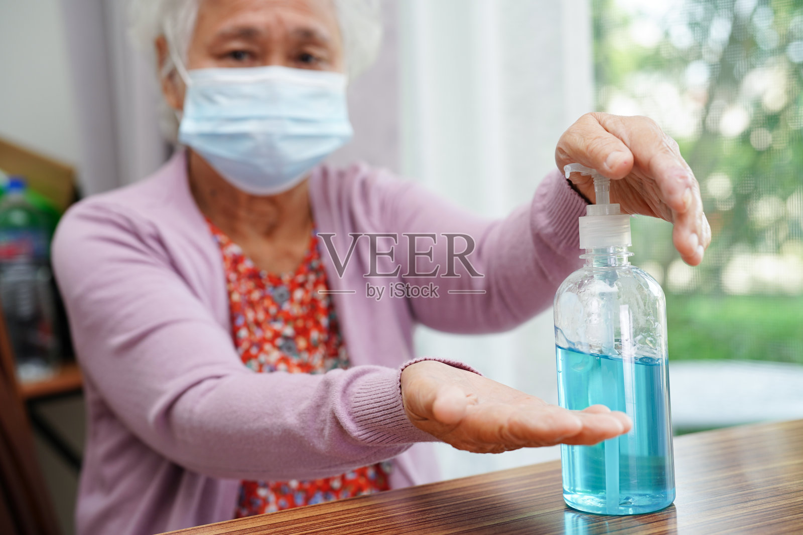 亚洲老年妇女按蓝色酒精洗手凝胶防止感染冠状病毒。照片摄影图片