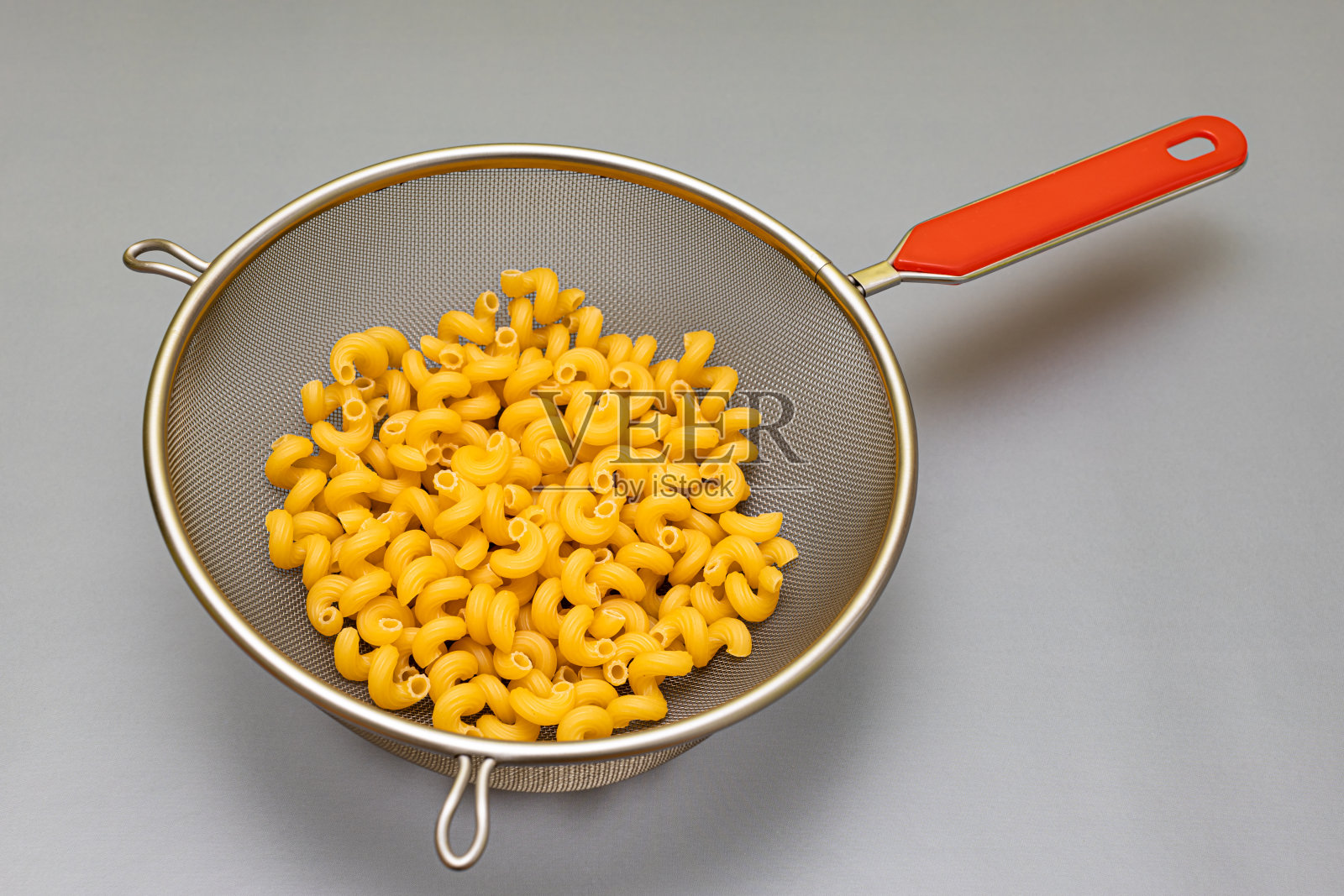 有红色把手的滤锅，里面的意大利面呈螺旋状照片摄影图片