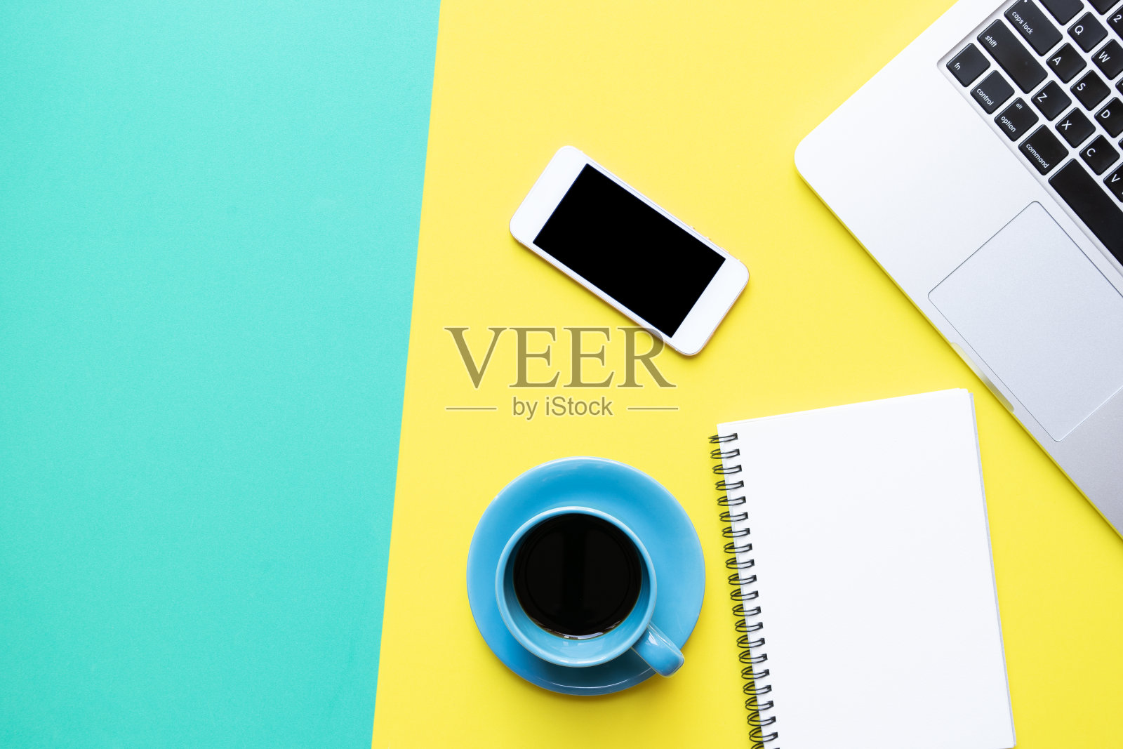 办公室背景黄绿相间的桌子上摆放着咖啡杯、笔记本、电脑和手机照片摄影图片