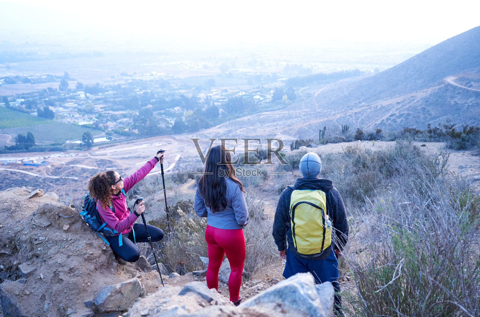 后视图组的三个拉丁裔徒步旅行者在山顶上看着地平线和探索与城市景观的地方照片摄影图片