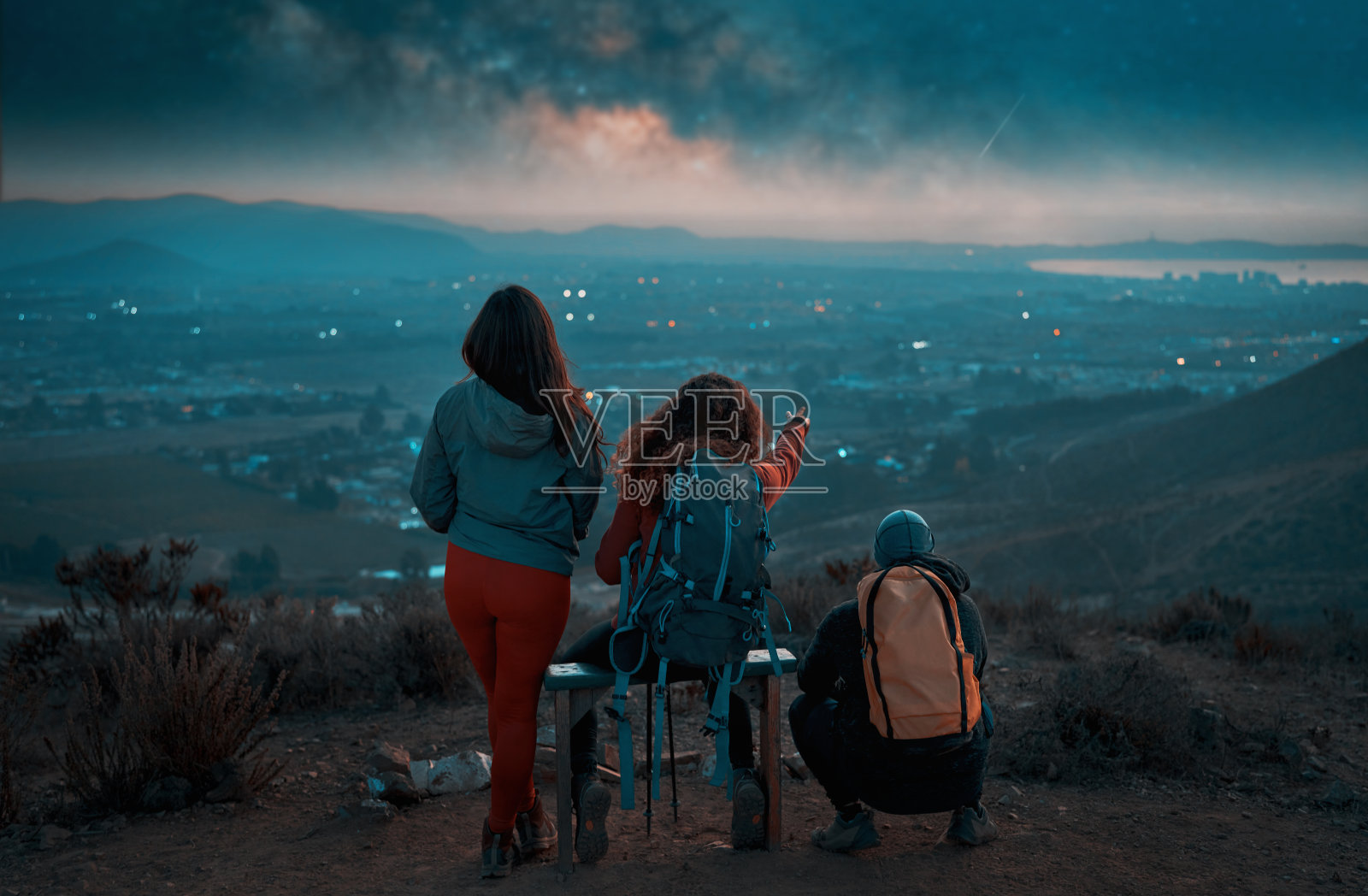 后视图混合组三个徒步旅行者在顶部看着地平线和银河在城市照片摄影图片