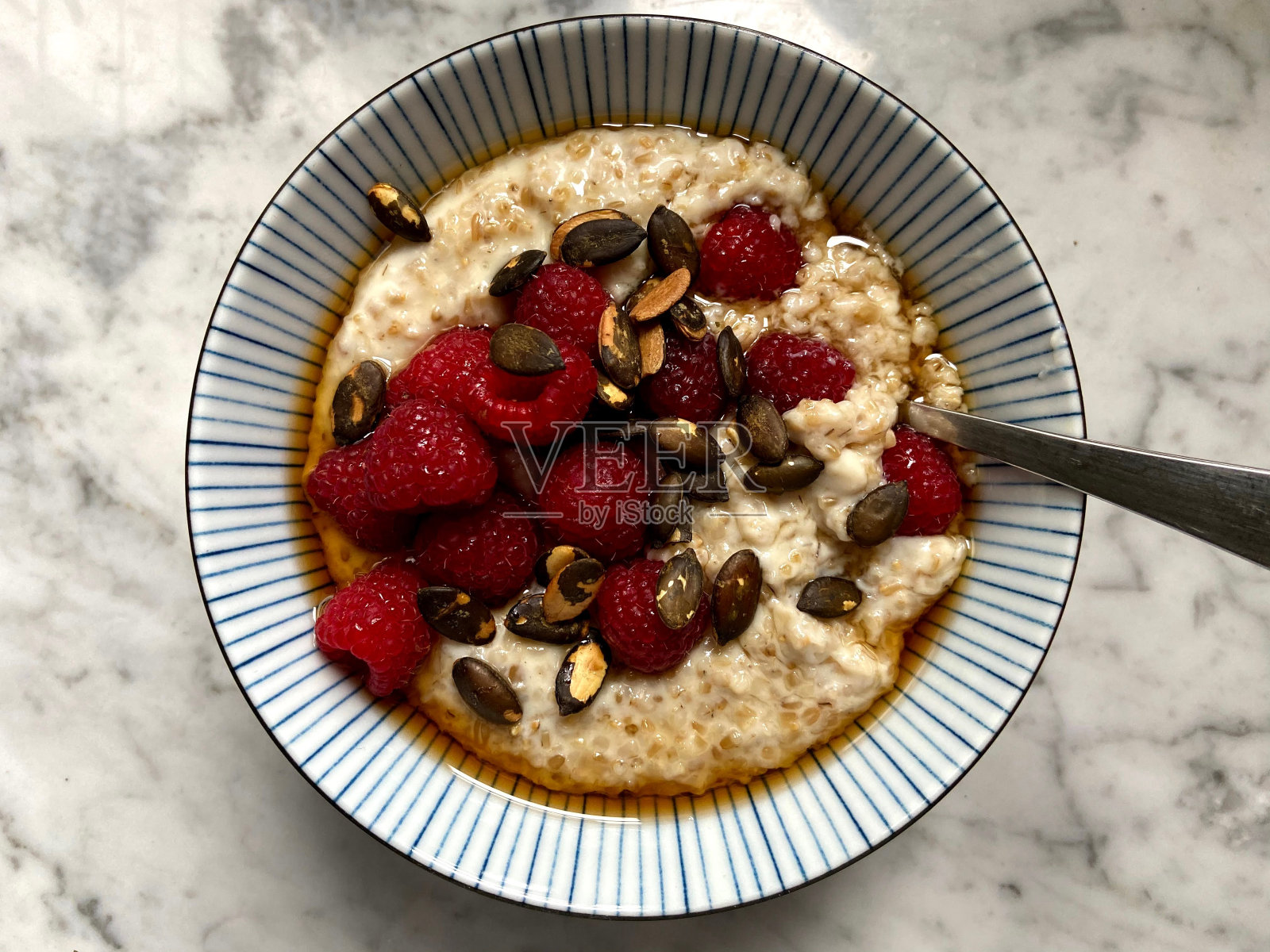 一碗煮熟的燕麦片，配上覆盆子、南瓜子和枫糖浆，放在条纹碗里照片摄影图片