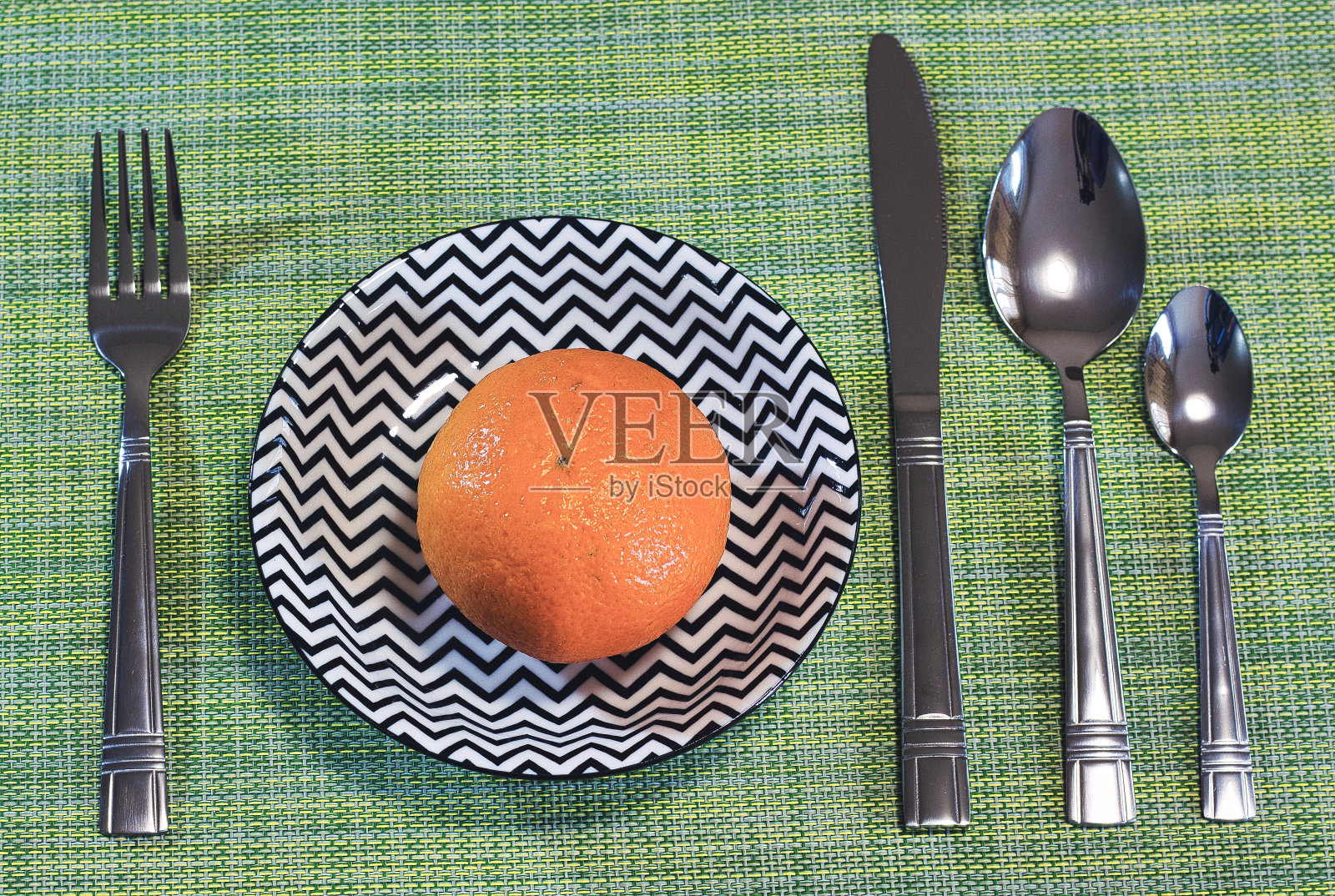 严格素食。一个小柑橘放在盘子里。绿色背景的餐具。柑橘类。照片摄影图片