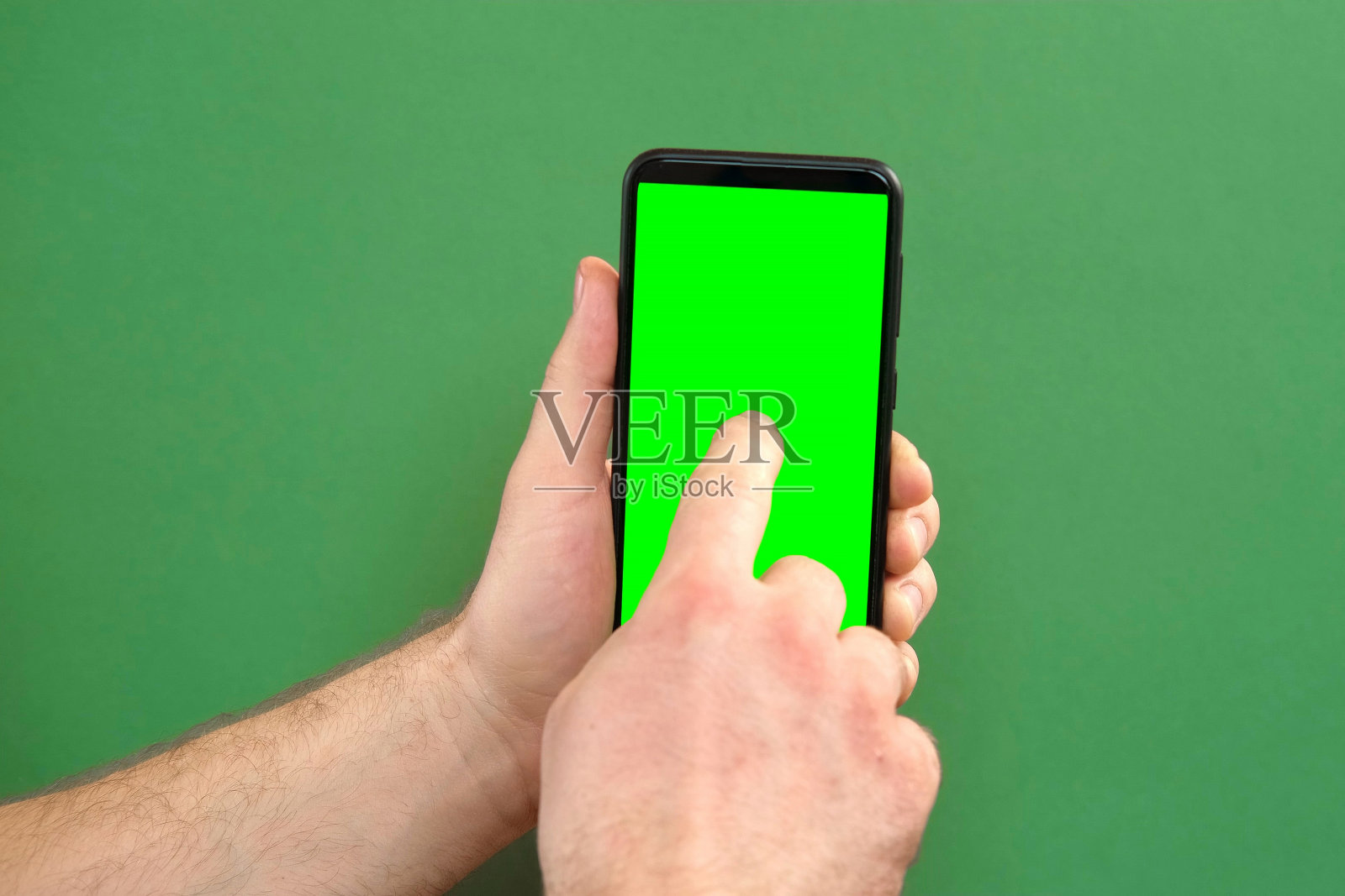年轻人手持绿色背景的绿屏智能手机。手势。男性用手触摸，点击，敲击，滑动黑色手机的彩色显示屏。关闭设备。现代科技照片摄影图片