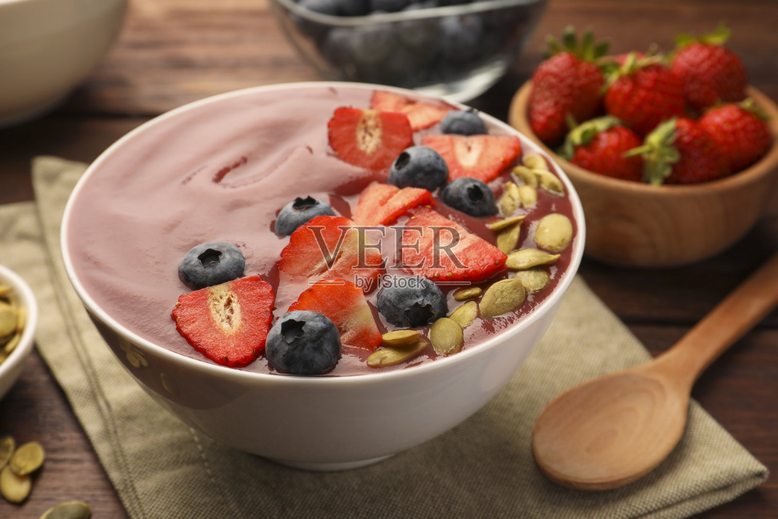 一碗美味的冰沙配上新鲜的蓝莓，草莓和南瓜子放在木桌上，特写照片摄影图片