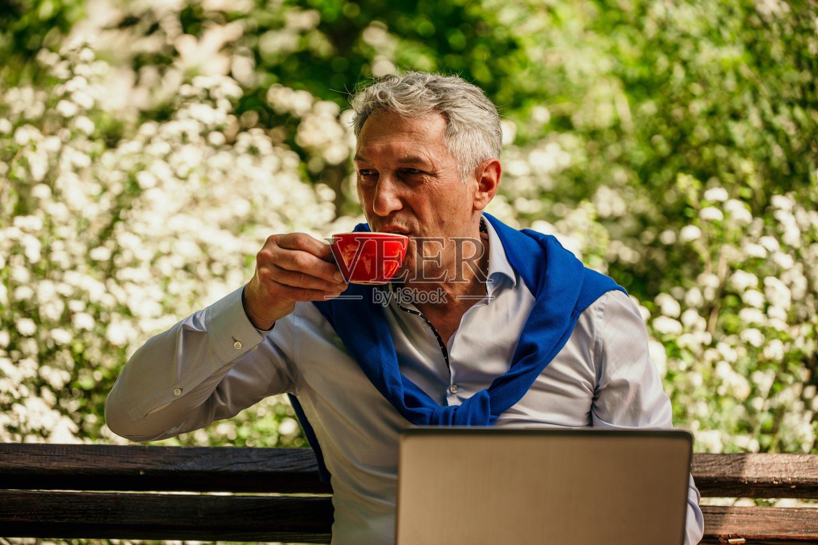 一个成熟的成年人坐在户外，使用笔记本电脑，喝咖啡和橙汁。照片摄影图片