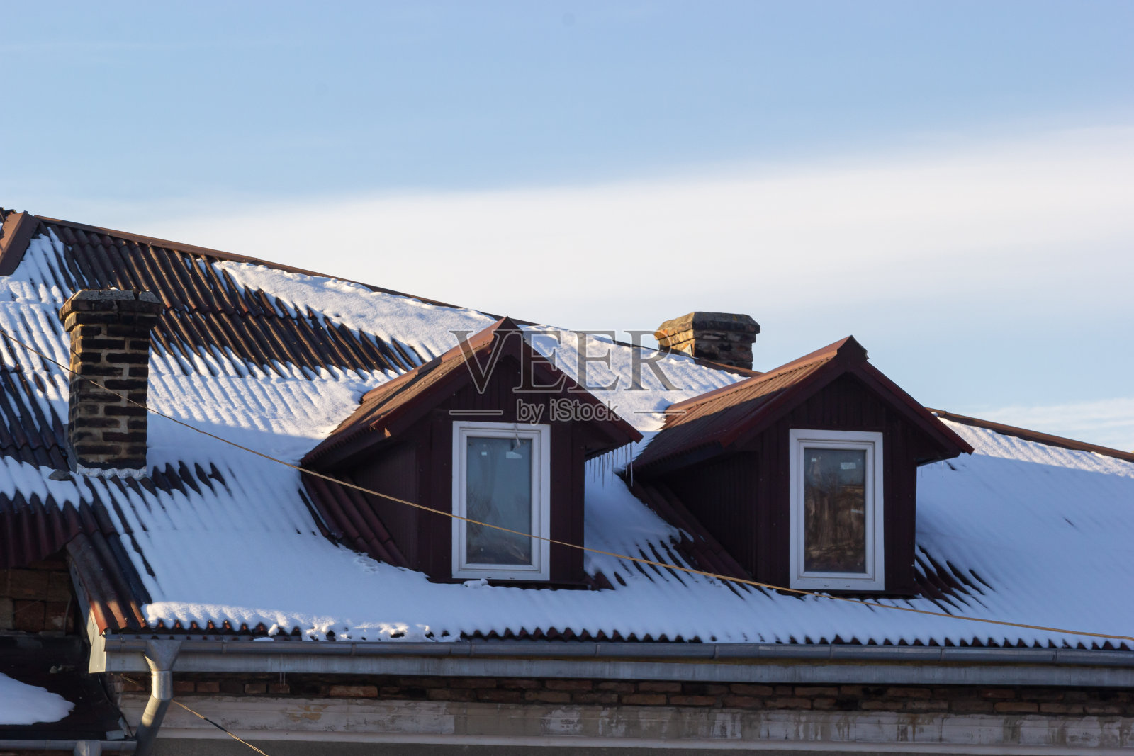 雪落在一座欧洲房子的红棕色金属瓦屋顶上照片摄影图片