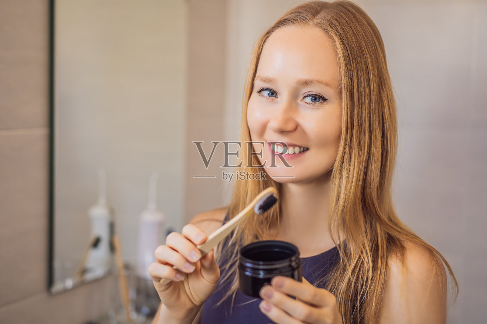 一名年轻女子在浴室里用含有活性炭的黑色牙膏和黑色牙刷刷牙照片摄影图片