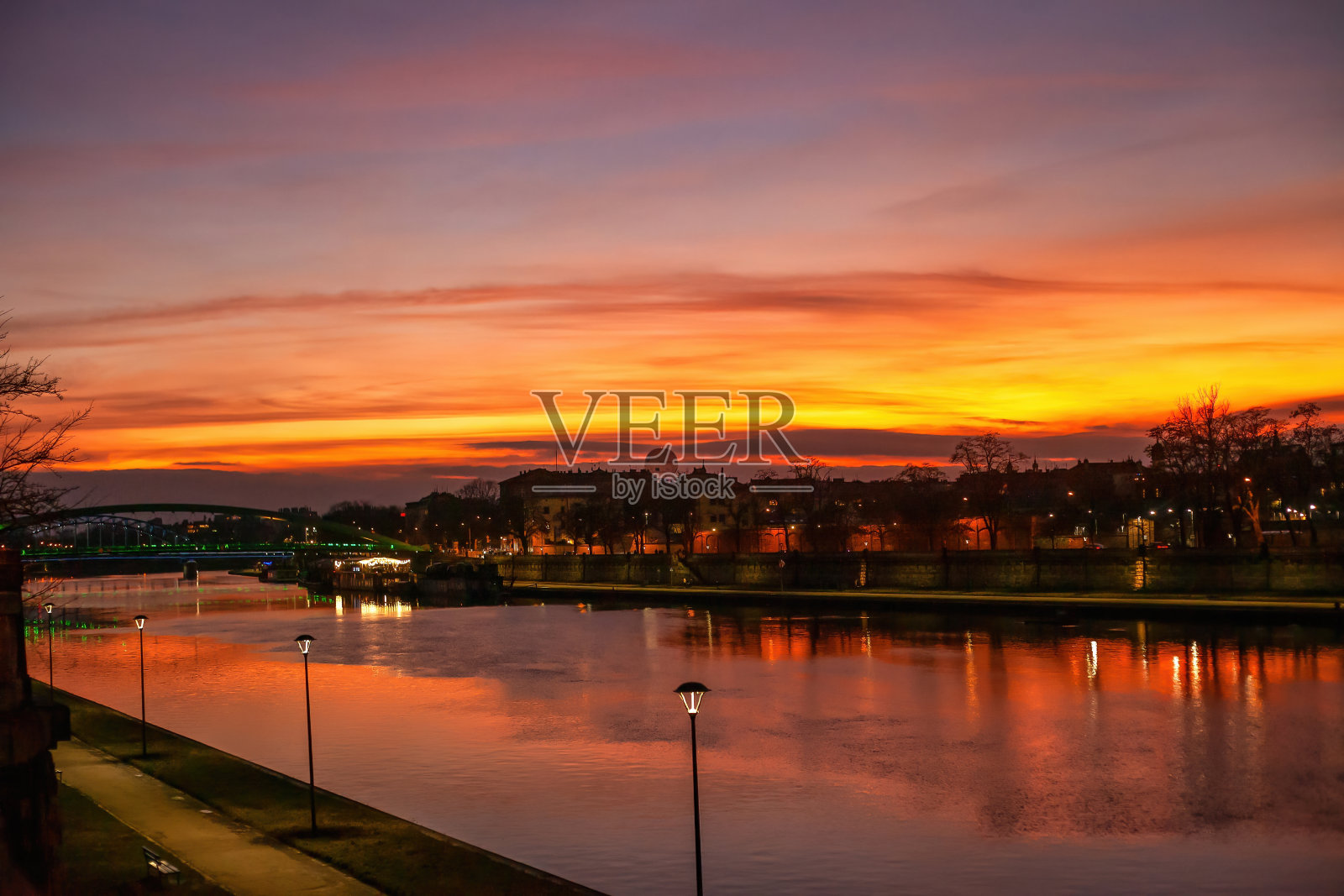 波兰克拉科夫维斯瓦河上明亮的夕阳。橙色晚霞映衬出黑色的桥梁和房屋的剪影照片摄影图片