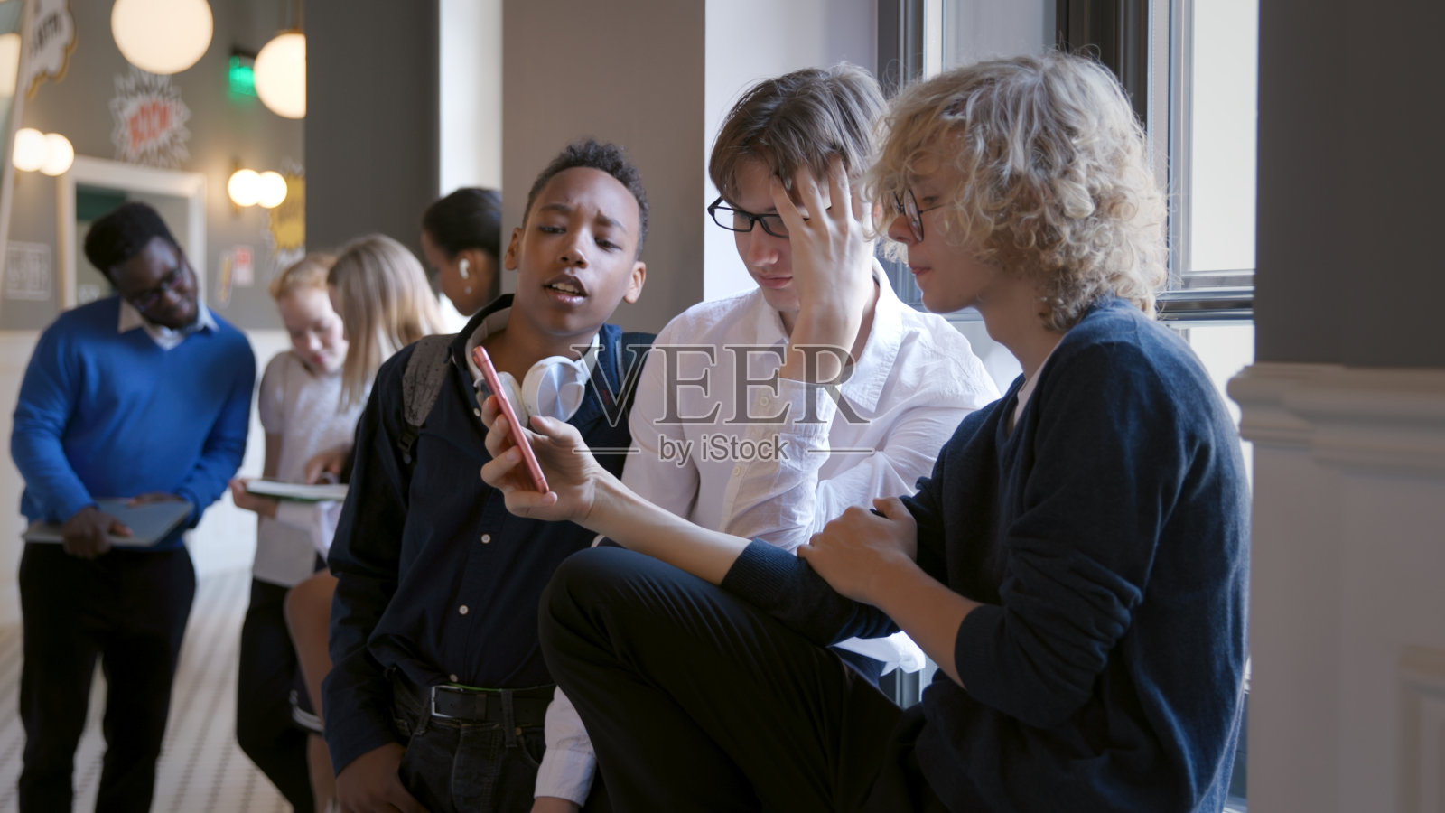 多种族青年朋友坐在学校走廊的窗台上玩手机照片摄影图片