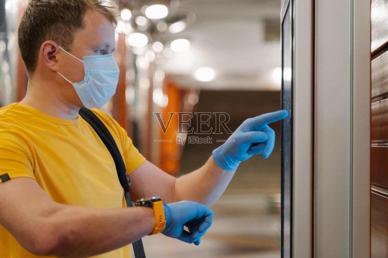 男子侧影查看手表上的时间，在防护橡胶手套上使用触摸屏，避免传播冠状病毒，大流行时间，戴医用口罩。卫生保健，检疫，病毒爆发照片摄影图片