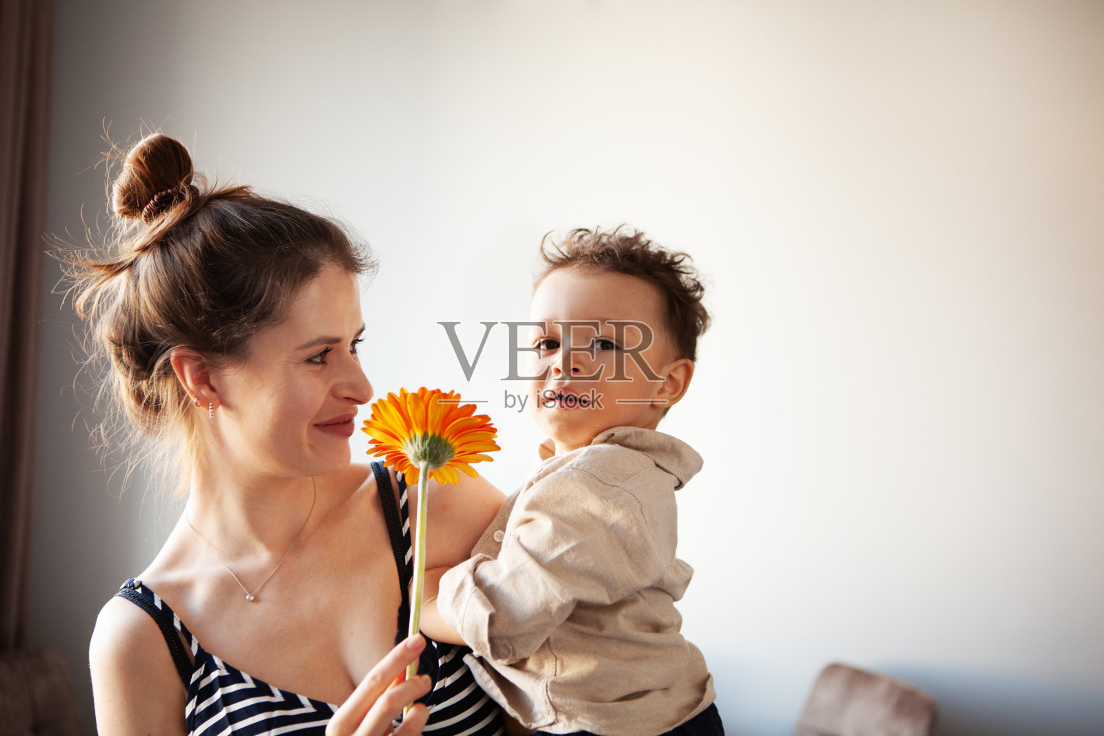真实的母亲抱着孩子，手握鲜花凝视着镜头。浅色背景下的真实生活和真实性照片摄影图片