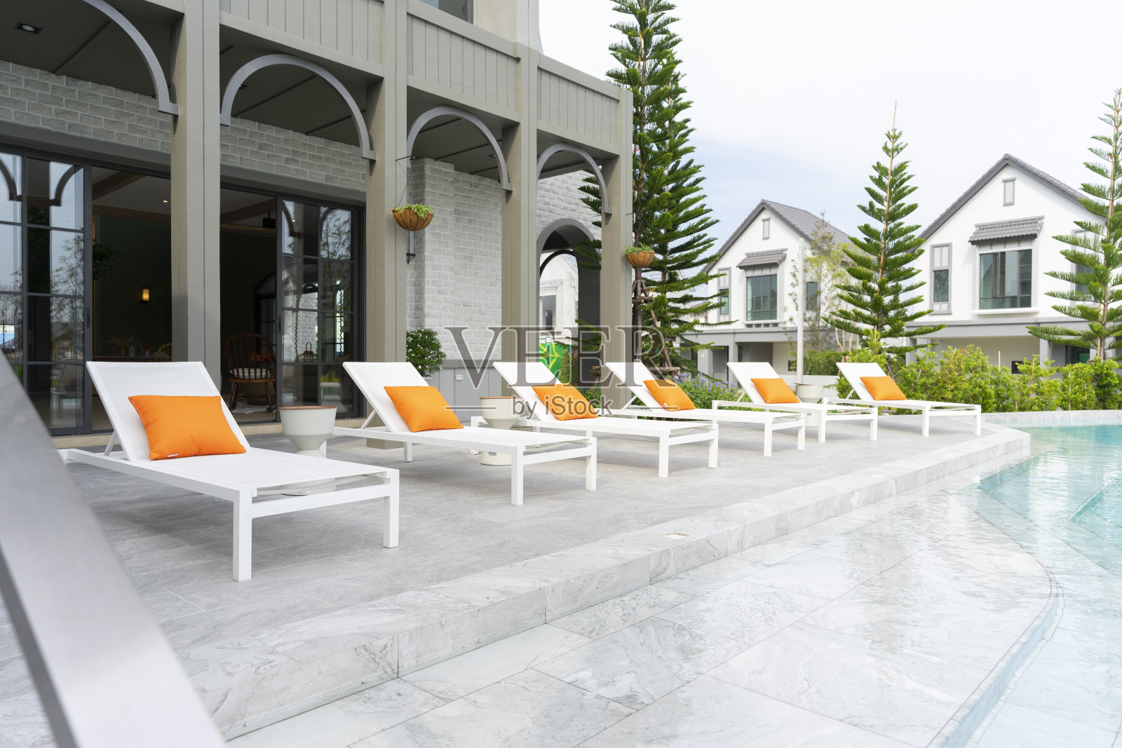 泳池边的白色躺椅和橙色枕头。照片摄影图片