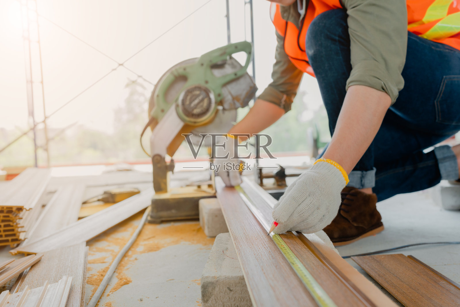 结构工人穿戴安全装备及安全帽从事建筑工作，并使用圆锯工作。照片摄影图片