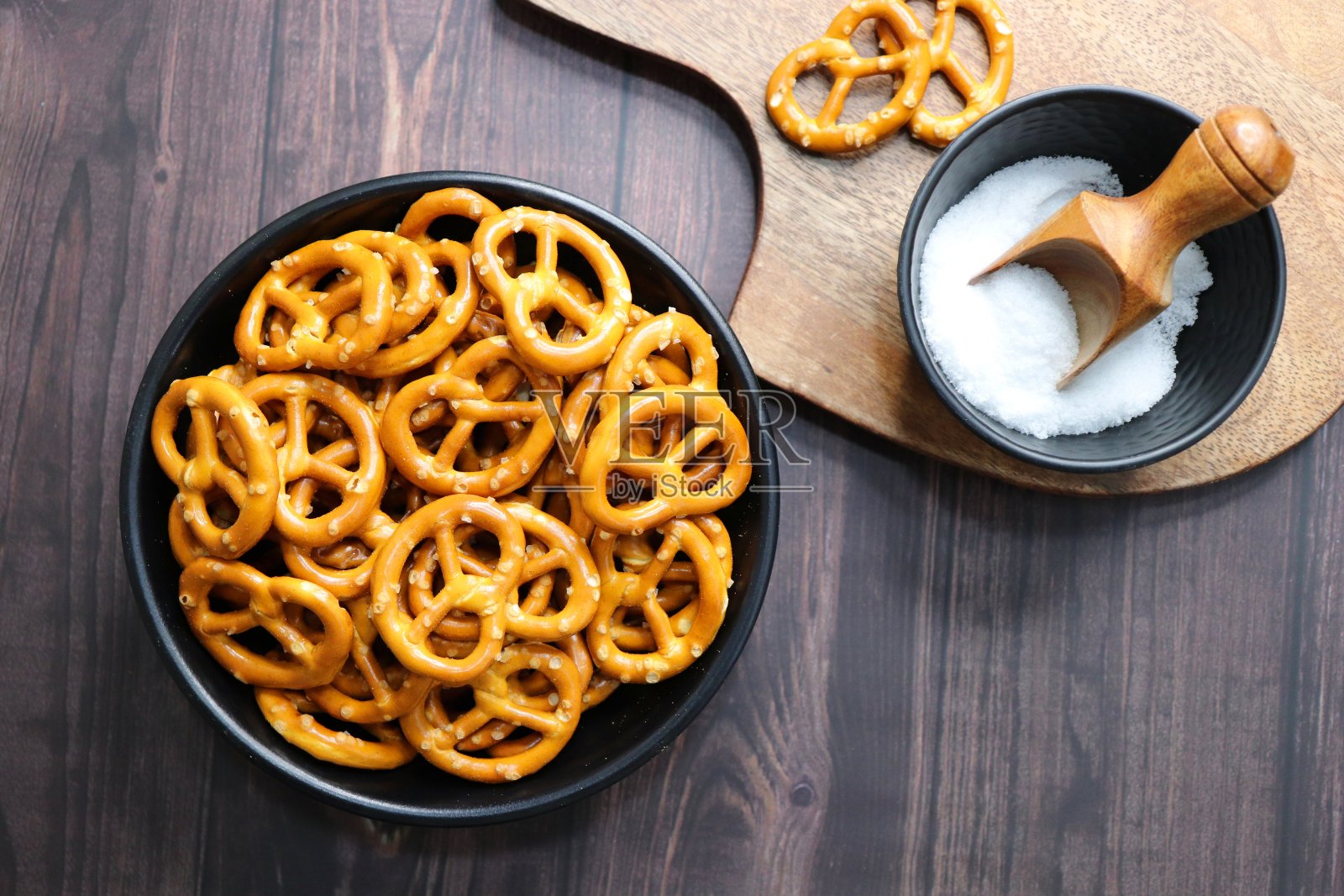 松脆的椒盐脆饼放在一个黑色的碗里，放在木桌上。完美的咸派对小吃。副本的空间。脆脆的咸饼干或饼干照片摄影图片