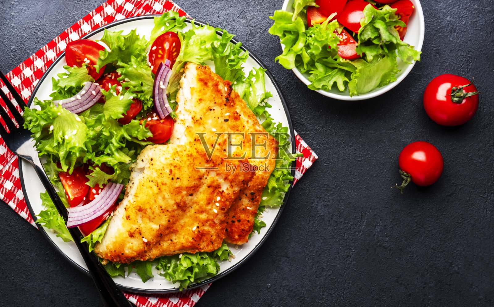 用生菜、圣女果和红洋葱做成的蔬菜沙拉炒白鱼片，黑色桌面背景，俯视图照片摄影图片