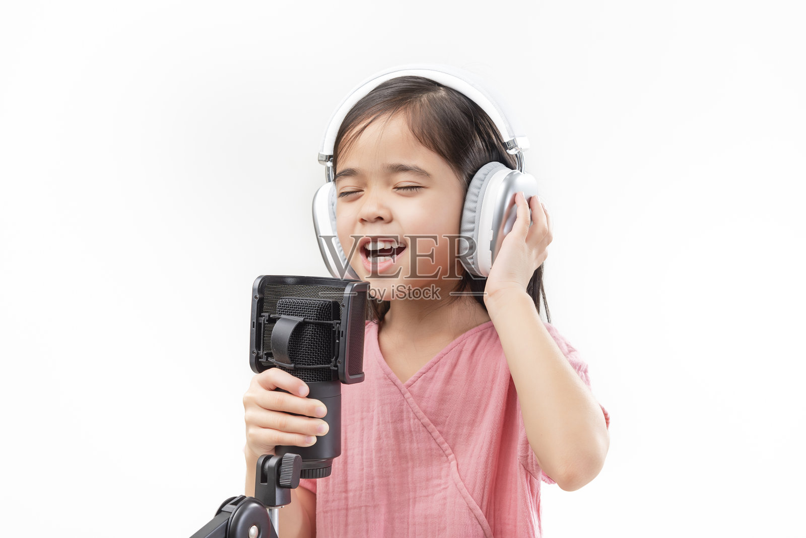 小女孩戴上耳机对着麦克风唱歌。照片摄影图片