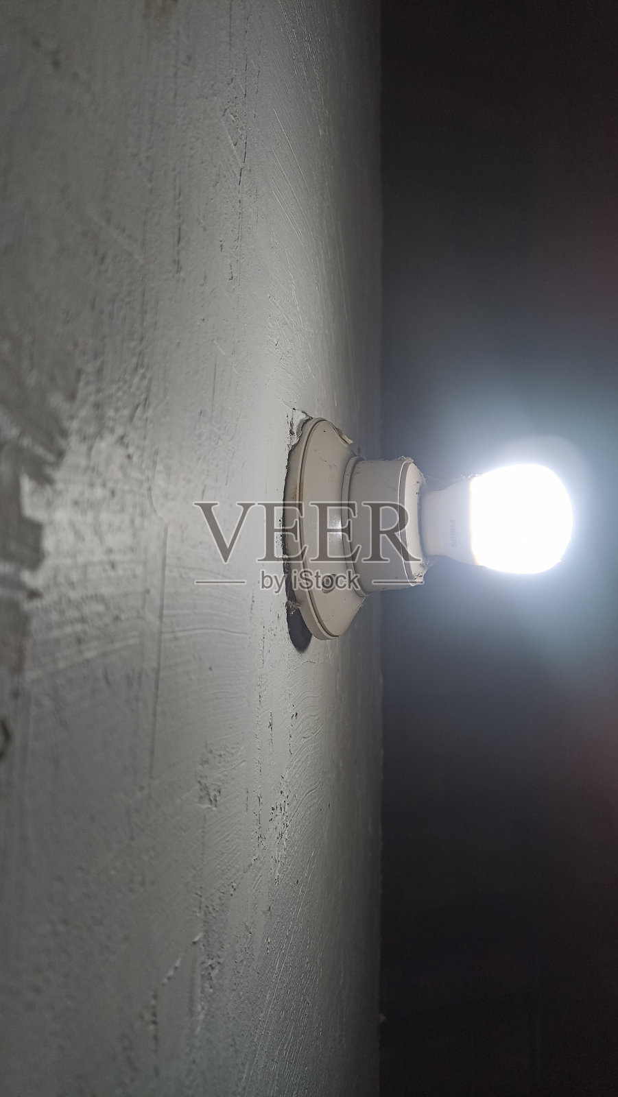 白色天花板背景上的灯泡。白色的led灯泡照亮了白色墙壁上的纹理。一个光秃秃的灯泡照亮了白色墙壁上的纹理。照片摄影图片