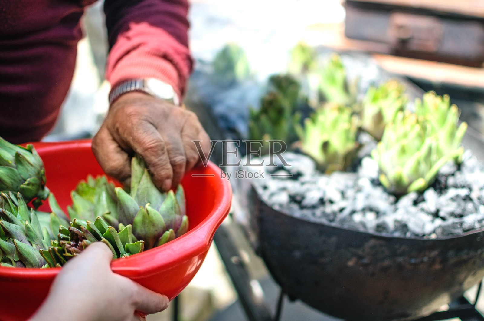 年轻的手把洋蓟放在红碗里递给年长的手照片摄影图片