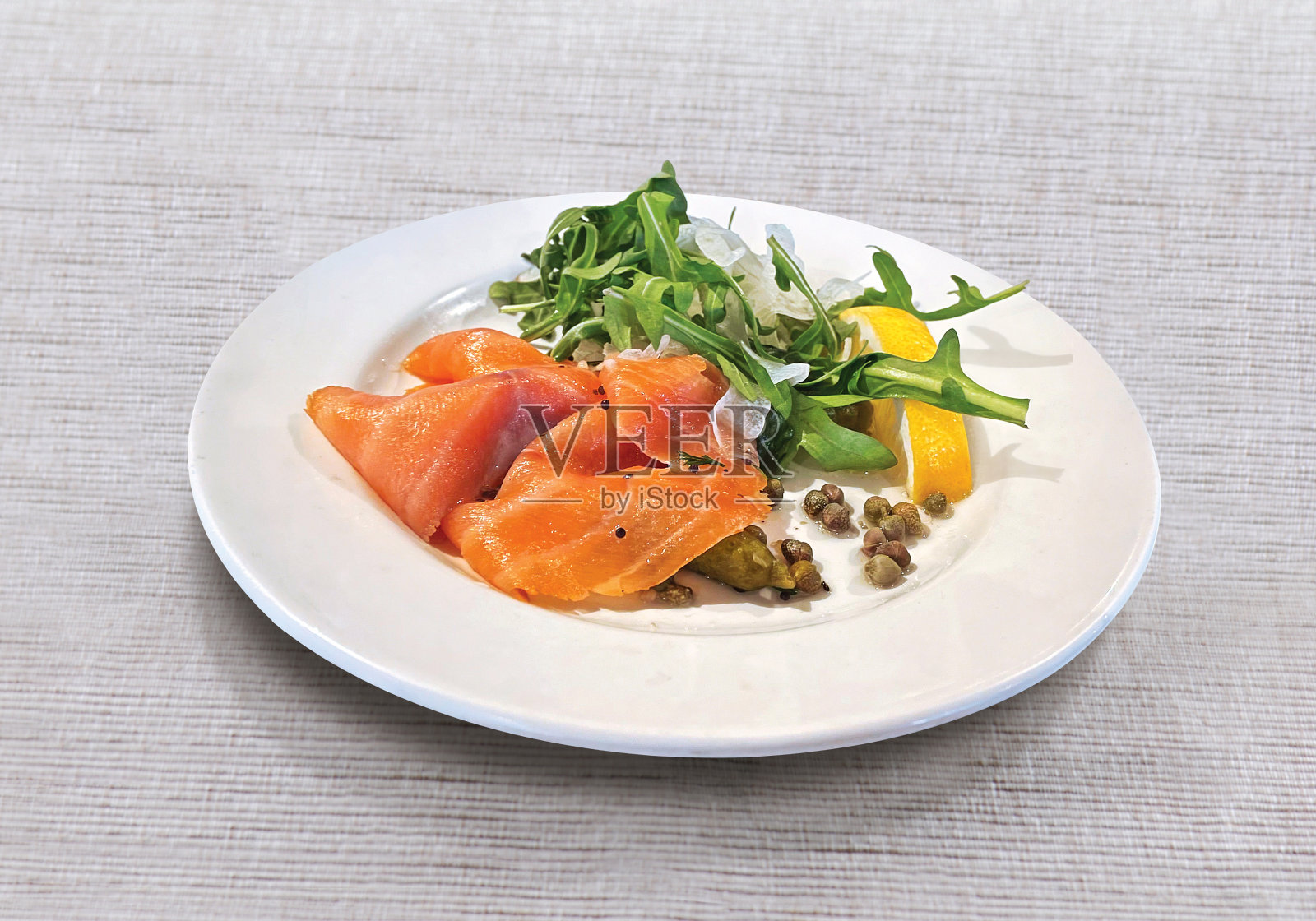 三文鱼片配芝麻菜，柠檬，腌黄瓜和酸豆，白色盘子照片摄影图片