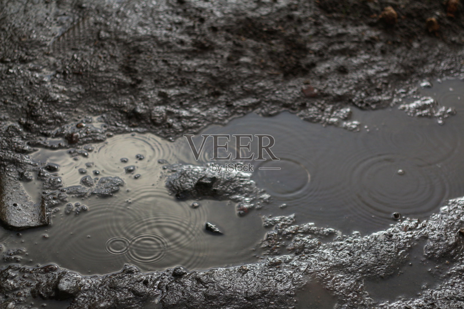 多雨的土壤。散焦的水滴溅在地上的水坑里。黑暗，悲伤，喜怒无常和戏剧性的背景。水波纹纹理。焦距不清照片摄影图片