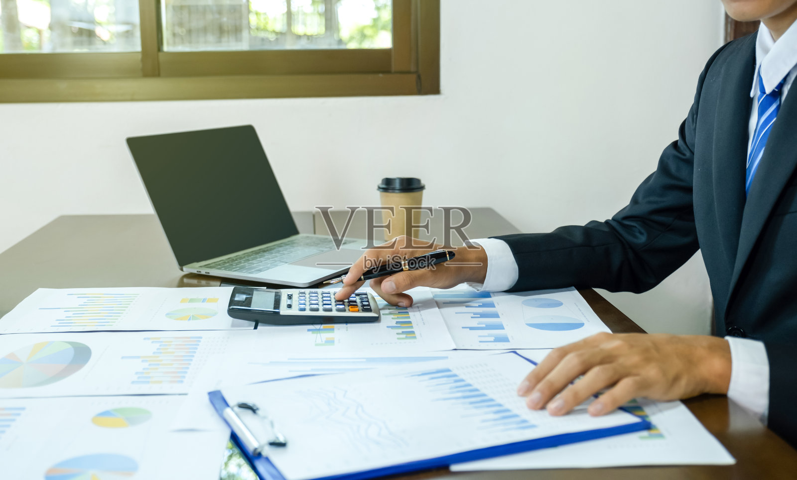 商人手持笔，使用计算器，在家庭办公室用笔记本电脑分析图表，设定具有挑战性的商业目标，并计划实现新的目标照片摄影图片