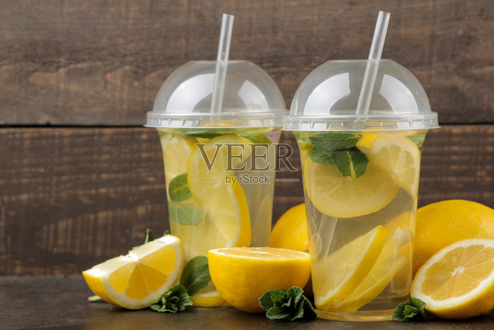 自制柠檬水，薄荷和柠檬装在塑料杯里，棕色背景。清爽的柠檬水饮料。照片摄影图片