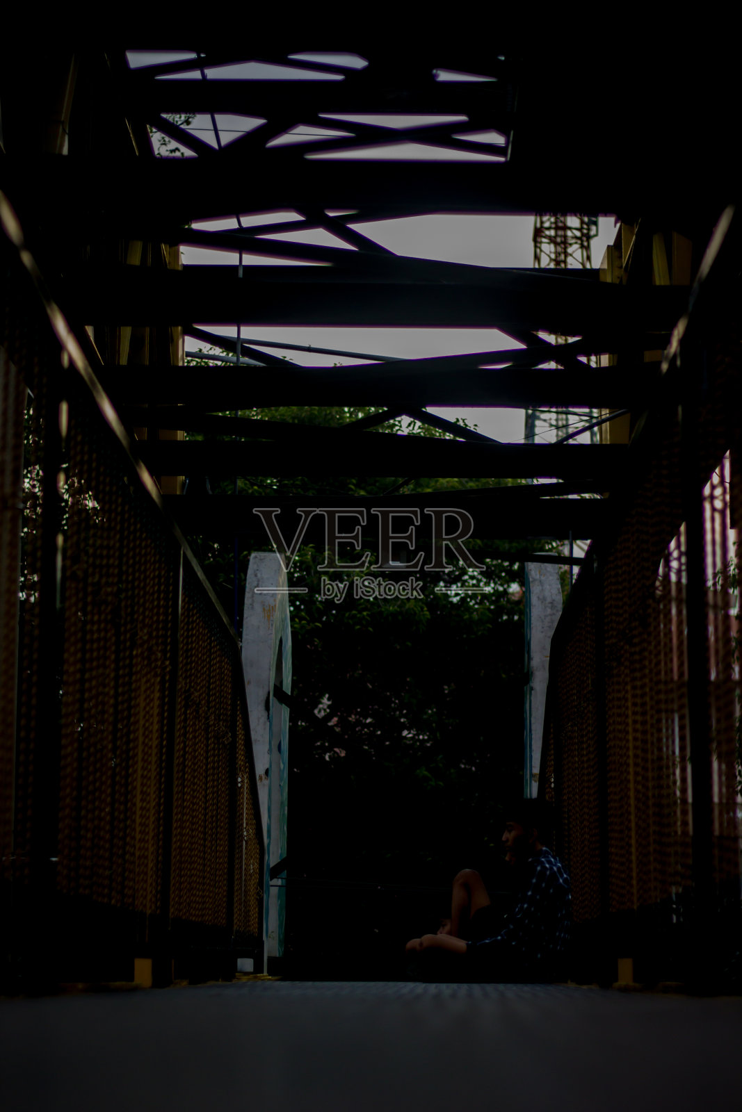 一个人坐在灯光昏暗的桥中央照片摄影图片