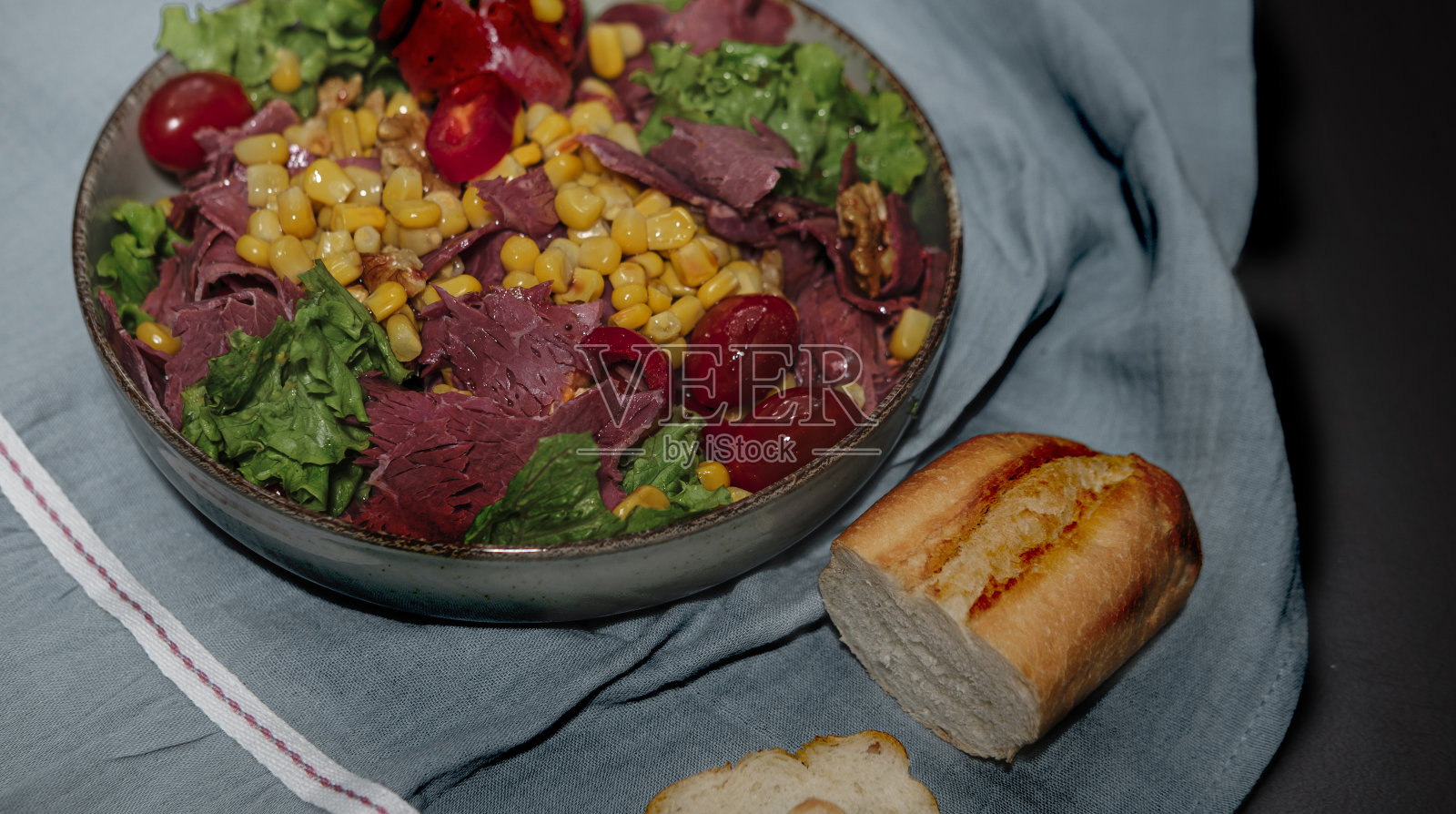冷切牛肉切片，清淡的夏季沙拉与绿色蔬菜，生菜，甜玉米，圣女果，法国法棍面包，熟食肉作为午餐零食或晚餐深色背景照片摄影图片