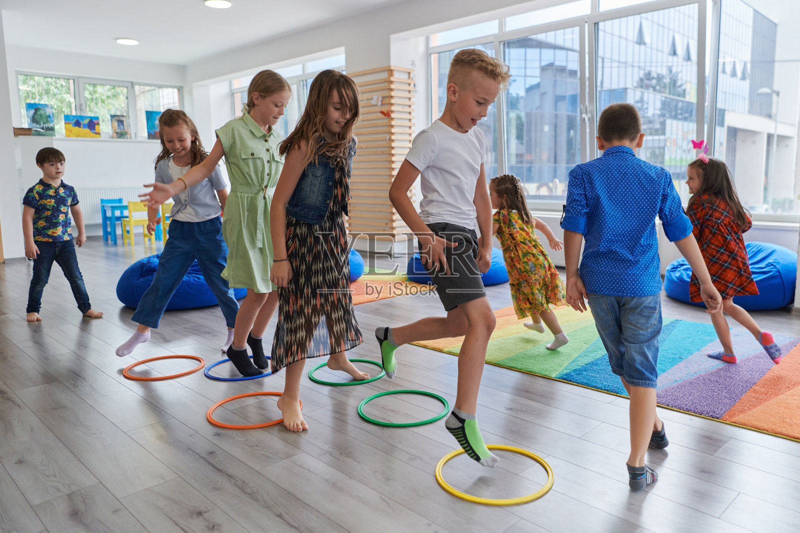 小幼儿园的孩子们带着女老师在教室室内地板上做运动。跳过呼啦圈在地板上绕圈。照片摄影图片