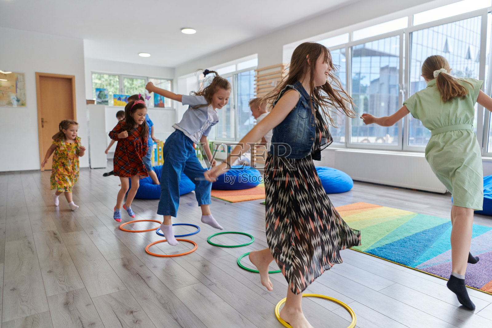 小幼儿园的孩子们带着女老师在教室室内地板上做运动。跳过呼啦圈在地板上绕圈。照片摄影图片