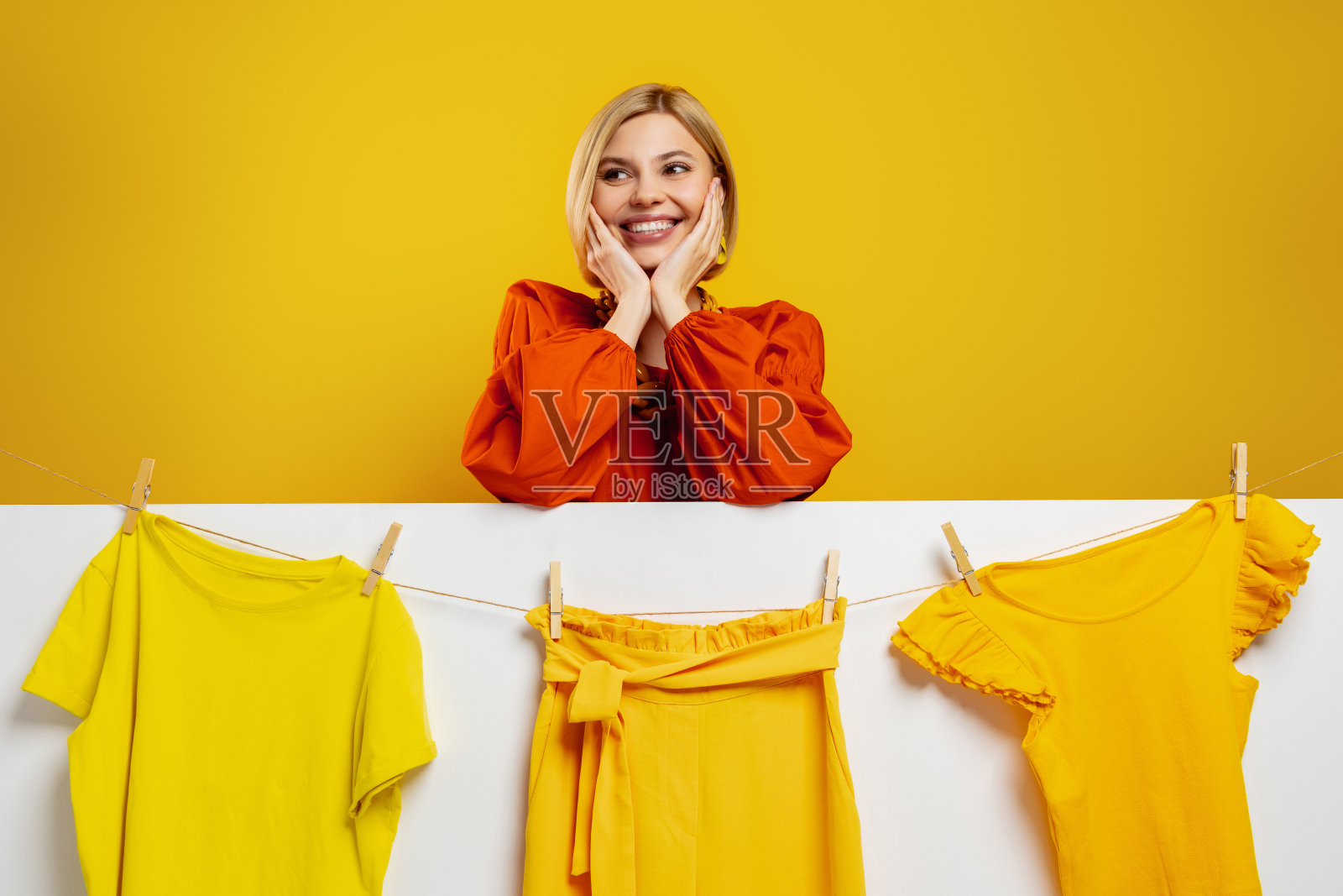 美丽的年轻女子对着挂在晾衣绳上的五颜六色的衣服微笑照片摄影图片