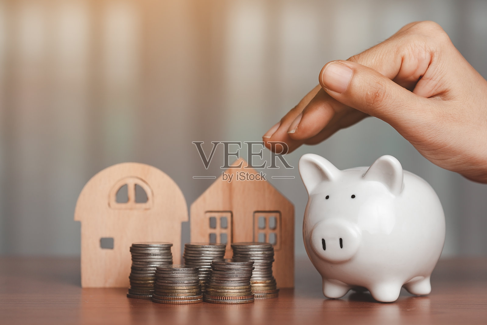 手捂着一个存钱罐，上面放着木屋模型，桌子上放着一堆硬币和钱照片摄影图片
