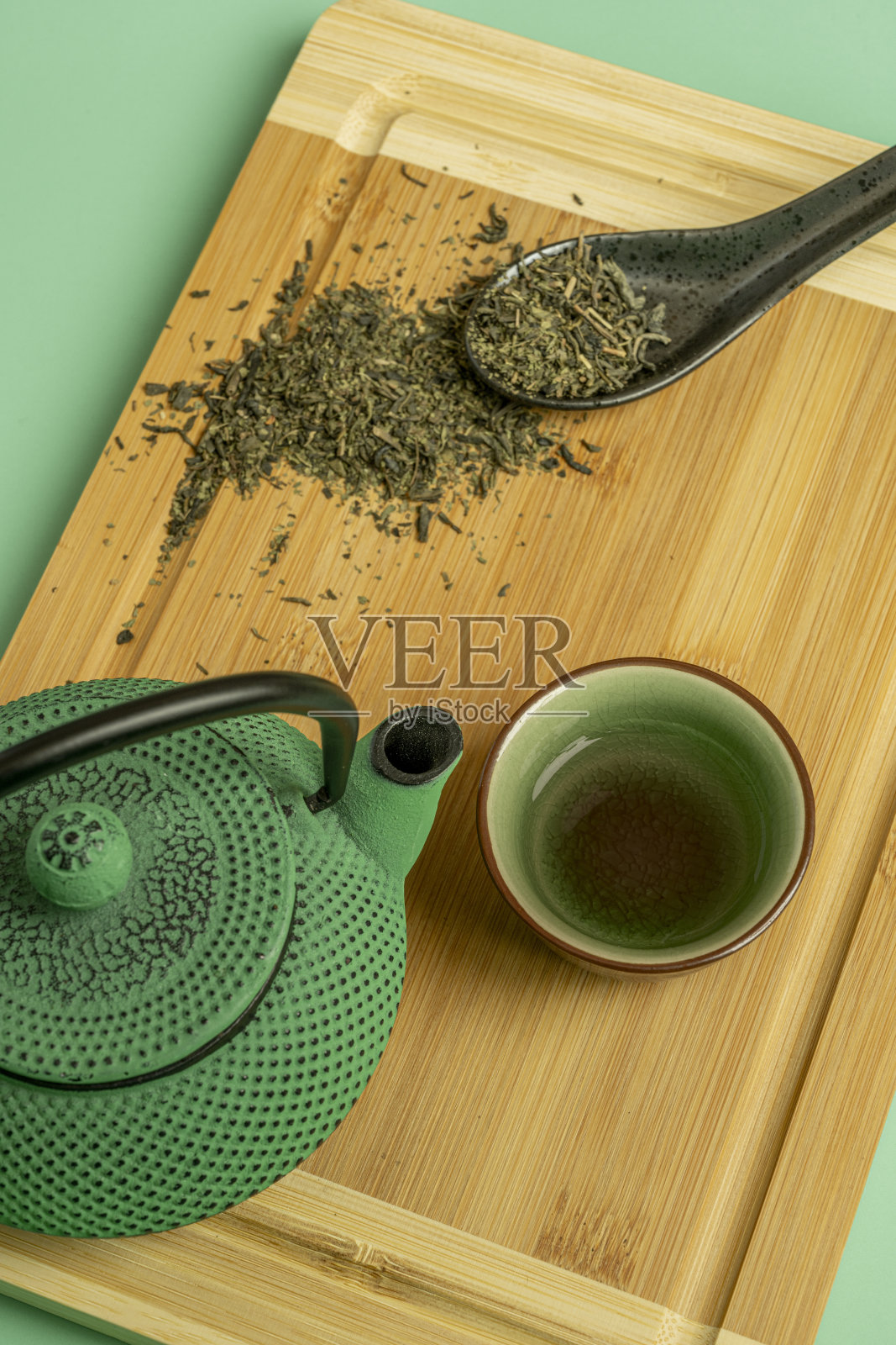 传统的绿色茶具和黑瓷勺的俯视图图像与干茶在棕色竹桌和绿色背景照片摄影图片