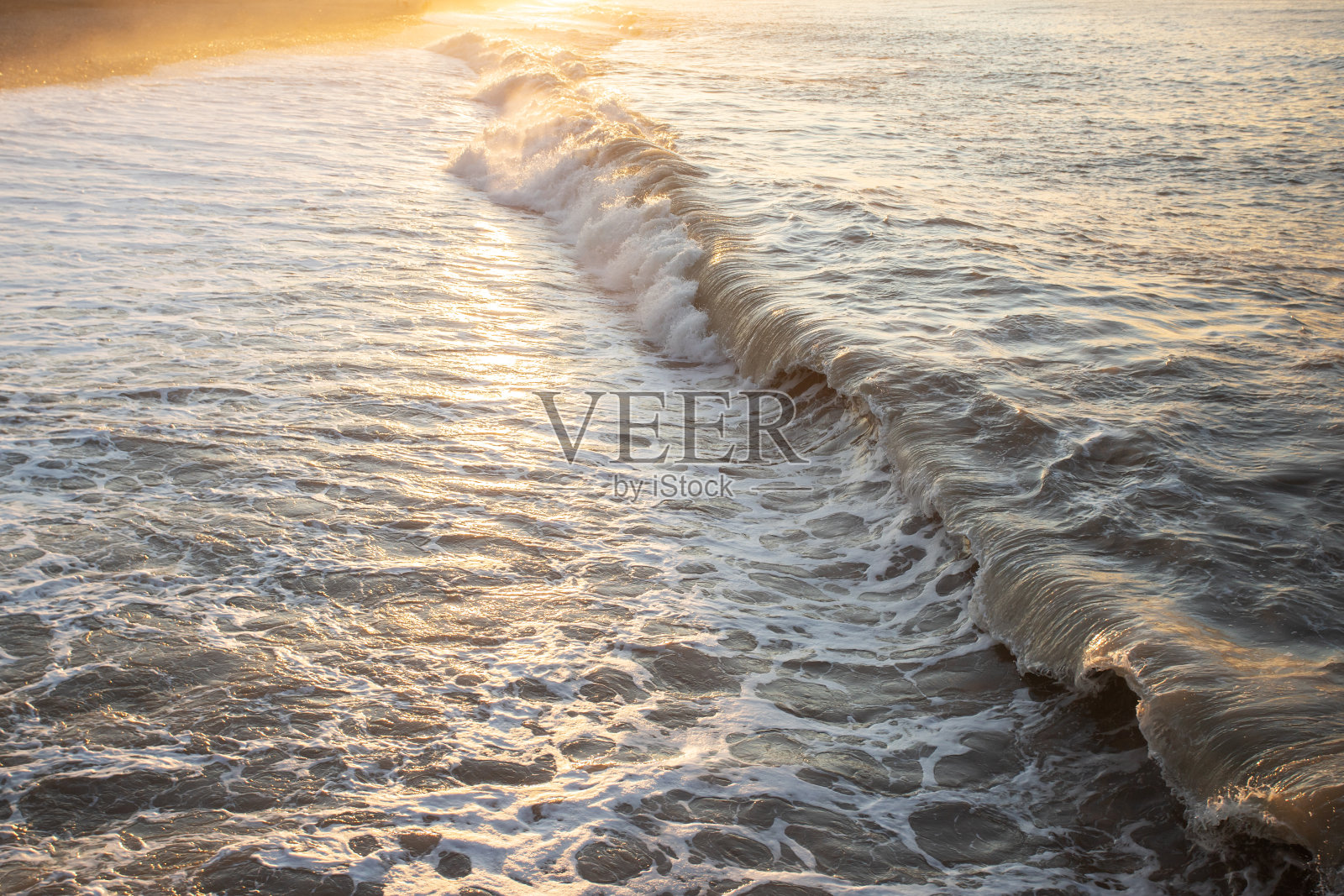 在日落的鹅卵石沙滩上溅起浪花照片摄影图片